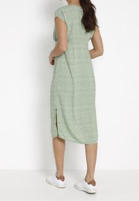 Robe midi verte à motif floral, manches courtes, taille cintrée et fentes sur les côtés. Associée à des baskets blanches pour un look décontracté.