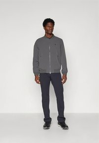 Hall sinine bomberjakk esilukuga, soonikkoes mansettide ja elastse vöökohaga, kombineeritud tumesiniste püksidega ja mustade tossudega.