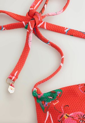 Piros, texturált pántok csomóval, színes virágmintával és egy kis Mikulás medállal díszítve. A szövet élénk és játékos.