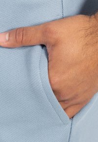Helles blaues Kleidungsstoff mit gerippter Textur; von Hand in die Seitentasche gesteckt. Verfügt über ein minimalistisches Design und eine eng anliegende Form.