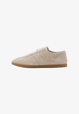 Zamszowe sneakersy w jasnym beżowym kolorze z białymi sznurowadłami, zaokrąglonym noskiem i gumową podeszwą z teksturowanymi detalami po bokach.