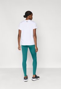 Λευκό αθλητικό πουκάμισο με κοντά μανίκια και λογότυπο στην πλάτη, συνδυασμένο με τιρκουάζ κολάν και μαύρα αθλητικά παπούτσια με λευκές σόλες.