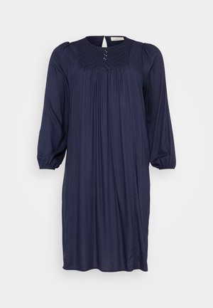 Robe bleu marine avec un décolleté arrondi, un devant plissé et des manches bouffantes trois-quarts. Dotée de petits clous décoratifs le long du décolleté.