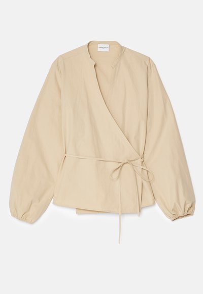 Beige wikkelbloes met lange puffmouwen, een V-halslijn, zijstrikdetails en een ontspannen pasvorm, gemaakt van een lichte katoenstof.