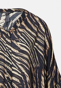 Blusa in stampa animale nero e crema con scollatura a V, chiusura a bottoni e vestibilità ampia, caratterizzata da una superficie liscia e un tessuto fluido.