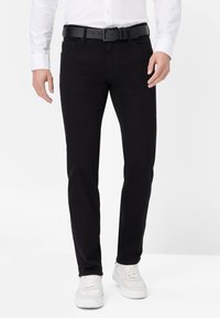 Jeans in denim nero con una vestibilità slim, design a cinque tasche e dettagli di cucitura sottili, abbinati a una cintura nera e sneakers bianche.