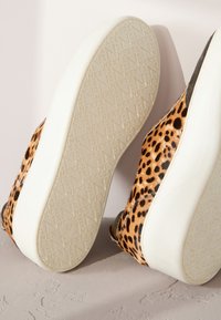 Chaussures à imprimé léopard avec une texture lisse, dotées d'une semelle en caoutchouc blanche et d'une tige douce ornée de motifs tachetés. La semelle présente des détails de marquage en relief.