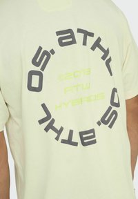 Helles gelbes Baumwoll-T-Shirt mit einem kreisförmigen grafischen Design in dunkelgrau und leuchtend gelber Schrift auf der Rückseite, mit einem lässigen Schnitt.