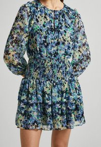 Długa sukienka z kwiatowym wzorem w odcieniach niebieskiego, zielonego i czarnego, z elastycznym pasem, falbanistym dołem i zapięciem na guziki przy dekolcie w kształcie łezki.