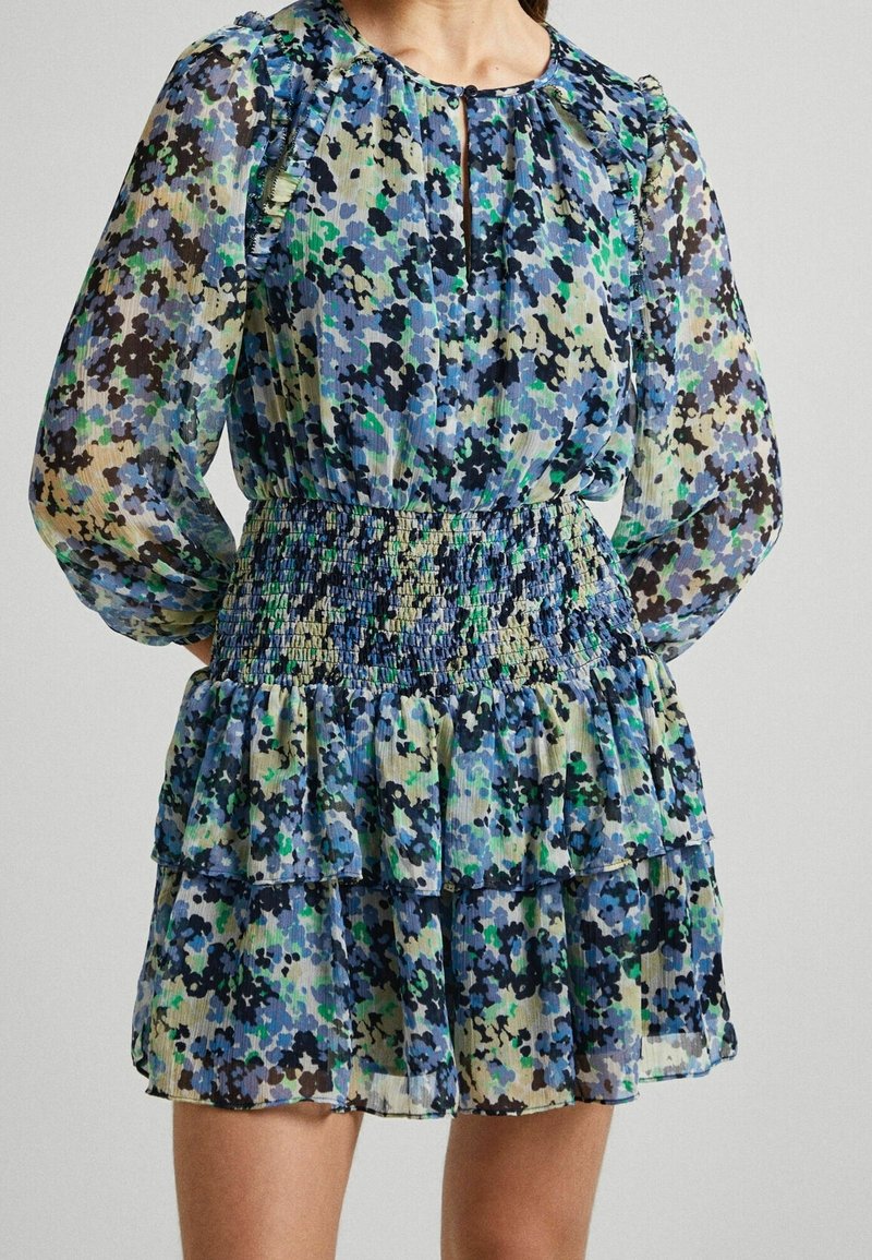 Długa sukienka z kwiatowym wzorem w odcieniach niebieskiego, zielonego i czarnego, z elastycznym pasem, falbanistym dołem i zapięciem na guziki przy dekolcie w kształcie łezki.