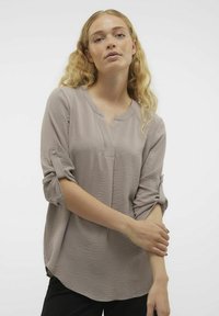 Blusa in taupe chiaro con finitura testurizzata, scollo a V, maniche arrotolate con bottoni e vestibilità rilassata.
