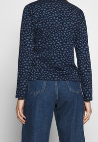 Maglietta a maniche lunghe blu navy con un tessuto testurizzato e a pattern; abbinata a jeans in denim blu a vita alta con tasche posteriori angolate.