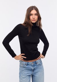 Zwarte coltrui van zachte stof met lange mouwen. Draagt met lichtblauwe, high-waisted spijkerbroek met een relaxte pasvorm.