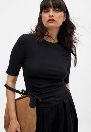 Black ribbed short-sleeve top with a round neckline, paired with a tan suede bag featuring a black leather strap and gold hardware accents.