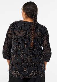 Čierna blúzka s kvetinovou sametovou textúrou a vzorom ruží, dlhými rukávmi a voľným strihom. Chrbát má jemný detail s plisovaním.