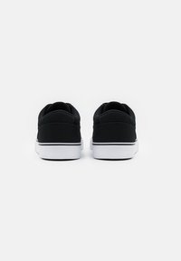 Černé plátěné tenisky s nízkým střihem, bílé gumové podrážky a černé detaily podél okrajů. Jednoduchý a minimalistický styl.