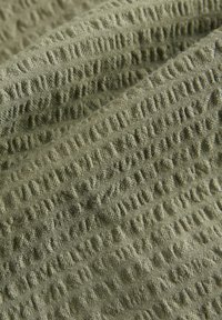 Tissu vert texturé présentant un motif en relief, mettant en valeur une apparence douce et tissée avec des élévations tactiles irrégulières à la surface.