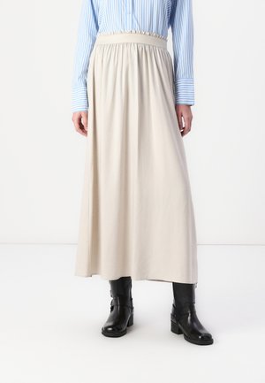 Maxi gonna beige chiaro con vita elastica, tessuto fluido e texture sottile, abbinarla a stivaletti neri. Camicia a righe blu visibile sopra.
