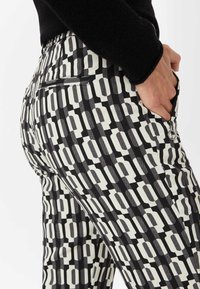 Pantalones estampados con un diseño geométrico en negro y crema, que cuentan con un bolsillo trasero y detalle de cremallera en el lateral para un cierre seguro.