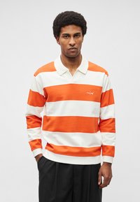 Polo de mangas compridas laranja e branco às riscas, com gola e logótipo bordado no peito, feito de tecido macio.