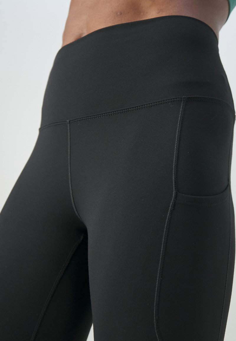 Leggings neri a vita alta con una texture liscia, dotati di cuciture piatte, una tasca laterale e un design aderente.