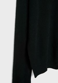 Tissu en tricot noir drapé avec une texture visible, montrant un bord légèrement courbé et des plis doux sur un fond clair.