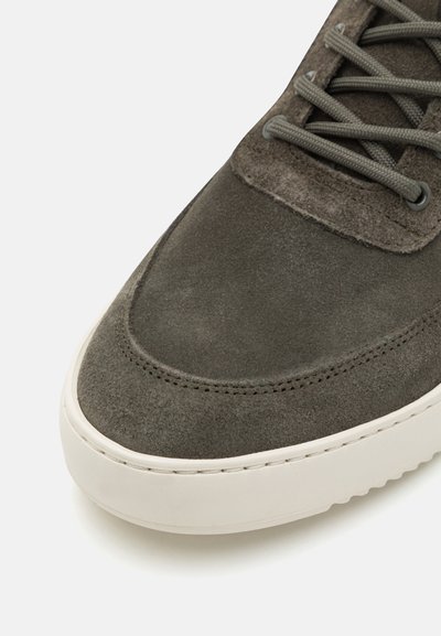 Gray suede sneaker close-up with a smooth rounded toe, textured upper, and contrasting off-white rubber sole. Simple, functional lace-up design.