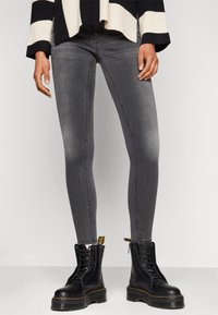 Gray denim skinny jeans with a faded texture, paired with black lace-up combat boots featuring yellow stitching and pull tabs.