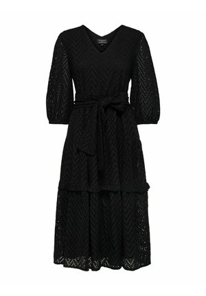 Zwarte kanten jurk met een V-hals, driekwartmouwen en een ceintuurlijf. Heeft een gelaagde rok met een zigzagpatroon.