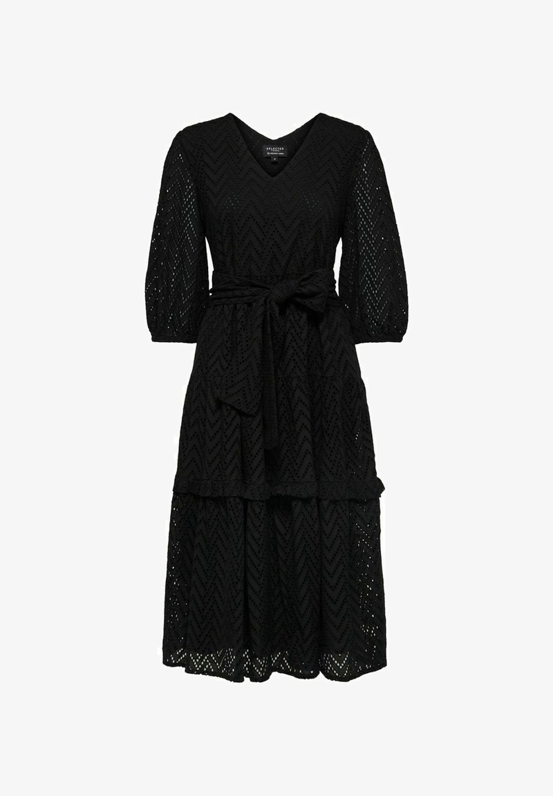 Musta pitsimekko, jossa on V-pääntie, kolmivartiset hihat ja vyötäröllä oleva vyö. Mekossa on kerroksellinen hame, jossa on chevron-kuvio.