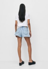 Farkkushortsit, joissa on repaleinen helma, vaalea sininen pesu ja takataskut, yhdistettynä valkoiseen t-paitaan ja mustiin paksupohjaisiin sandaaleihin.