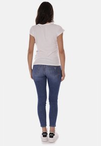 T-shirt bianco a maniche corte abbinato a jeans skinny blu. I jeans presentano un lavaggio sbiadito e due tasche posteriori. Le scarpe sono sneakers bianche.
