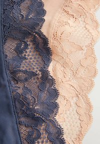 Lace stof in marineblauw en blush, met bloemmotieven en gegolfde randen. De textuur is verfijnd, met gedetailleerde borduursels en netvormige delen.