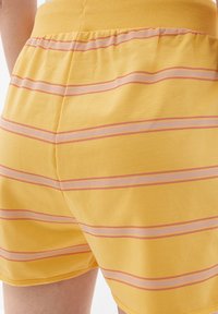 Gelbe Shorts aus weichem Stoff, mit horizontalen pinken und lila Streifen, elastischem Bund und entspanntem Schnitt.
