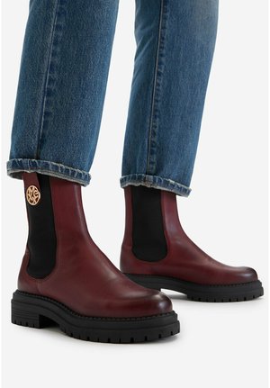 Knöchelhohe burgunderrote Lederstiefel mit schwarzen elastischen Seitenpaneelen und dicken schwarzen Sohlen, getragen zu blauen Jeans.