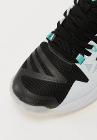 Zapatilla atlética en negro y azul claro con parte superior de malla, puntera de goma texturizada y gruesos cordones negros, con acentos de patrón distintivos.