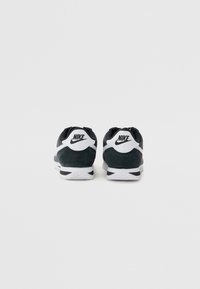 Fekete-fehér Nike tornacipő, velúr felsőrésszel, párnázott bokapánttal és hullámos mintázatú textúrált fehér talppal; logó a saroknál.