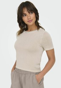Lys beige kortærmet t-shirt lavet af blødt stof, med rund halsudskæring og en tætsiddende silhuet, parret med løse lysegrå bukser.