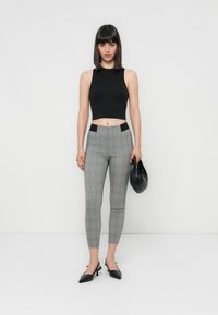Črna skrajšana majica brez rokavov, ujemajoča se s sivimi karirastimi slim-fit hlačami z črnimi pasom, ter črnimi petnimi mules čevlji. Drži črno torbico.