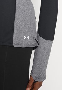 Langarm-Sportoberteil mit schwarzem Körper und grauen Ärmeln, aus strukturiertem Material und mit einem weißen Under Armour-Logo am Saum.