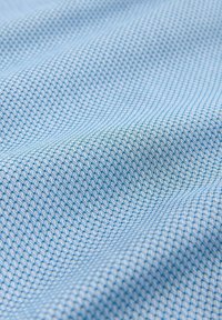 Tissu bleu clair en nid d'abeille avec une petite texture carrée en relief et des plis doux créant des ombres.