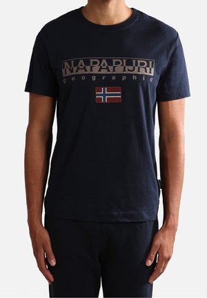 Mężczyzna noszący granatowy t-shirt Napapijri Geographic z naszywką norweskiej flagi w kolorach czerwonym, białym i niebieskim, umieszczoną na środku klatki piersiowej.