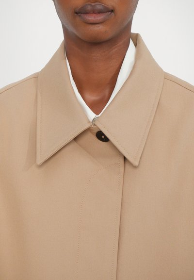 Beige coat with a wide collar, button closure, and textured fabric. Features a cream inner lining and visible stitching details.