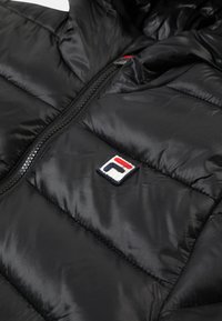 Giubbotto imbottito nero con design trapuntato, finitura lucida, zip completa e un piccolo logo ricamato in rosso, bianco e blu sul petto.