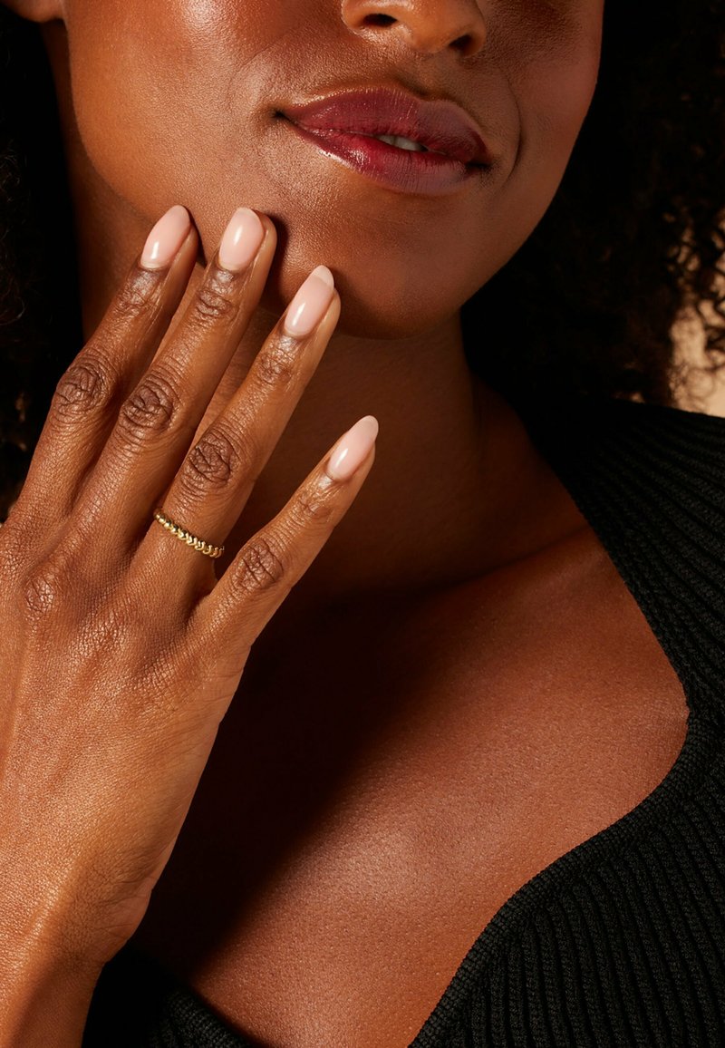 Gold ring on a fingers with almond-shaped, light pink nails. Smooth skin texture with a dark top having a ribbed pattern.
