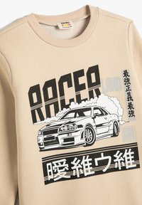 Beżowy sweatshirt z prążkowanym okrągłym dekoltem, z czarnym nadrukiem wyścigowego samochodu oraz stylizowanym tekstem w szaro-czarnych akcentach.