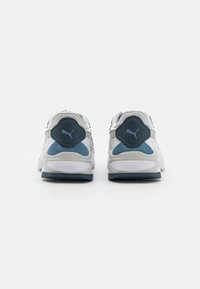 Zapatillas deportivas blancas y marinas con una parte superior de malla texturizada y acentos de ante. Presentan una suela acolchada y un logotipo prominente en el talón.