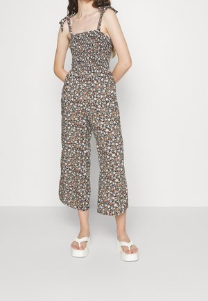 Kukkakuvioinen haalari mustalla taustalla, jossa on valkoisia ja oransseja kukkia, kirjailtu yläosa, leveät lyhyet lahkeet ja säädettävät nauhakiinnitykset.