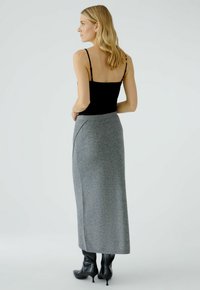 Top noir à bretelles et longue jupe grise en tricot avec un pli sur le côté. La mannequin porte des bottes à talons noires. Fond simple.