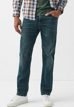 Donkerblauwe denim jeans met een recht model, lichte vervaging op de dijen en gestikte details bij de zakken, gecombineerd met witte sneakers.